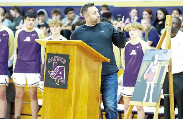 Tony Micheli points to the name of his childhood friend Brian Wilson, whose name hangs on a banner in the Alpine High School gymnasium, Friday night. Micheli organized the dedication ceremony for the Wilson-Stice memorial basketball court. Photo by Shawn Yorks