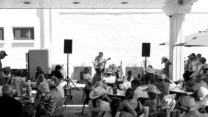 The lively crowd enjoyed the talent and humor of artist John Baumann while trying to escape the heat in the shaded patio. Baumann had the crowd swaying and sometimes laughing while they enjoyed barbeque and drinks. Photo by Joh Covington