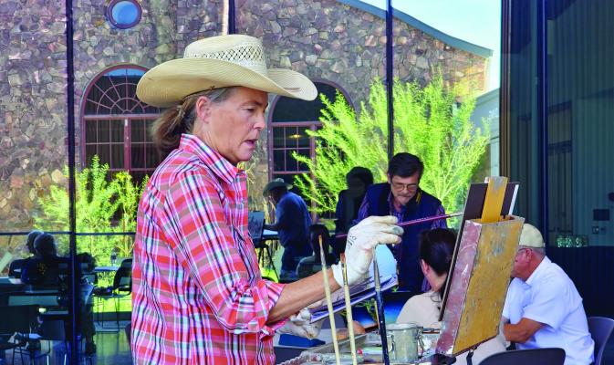 Trappings of Texas artist Alice Leese works to recreate a scene from a photograph of a recent cattle work on her family ranch. Leese, Kerri Menchaca (background), and Tim Oliver (reflection) were on the patio at the Museum of the Big Bend on Friday afternoon to exhibit their artistic process to onlookers. Photo by Kara Gerbert
